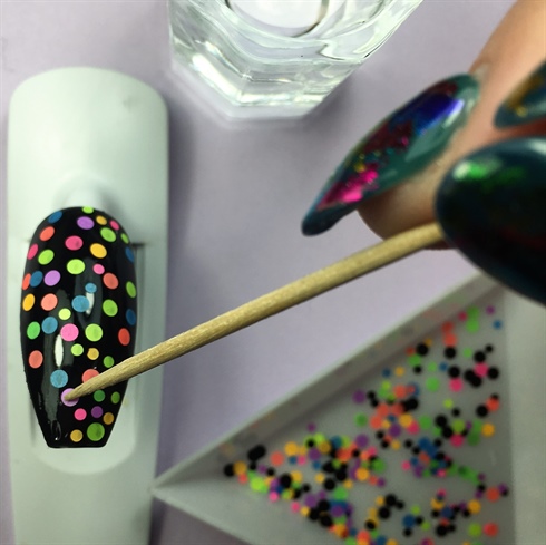 I applied multi-colored dots onto the tacky layer of black gel polish. I topped with a layer of base coat, cured, a layer of top coat, and then cured again. I then applied my 3-D elements using a small bead of clear acrylic. **HELPFUL HINT: Dip a toothpick in a dappen dish of water to easily pick up tiny glitters. 