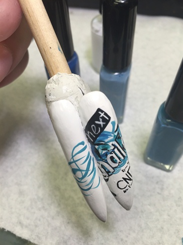 Using various blue stripers, make swirls. Using black and white nail polish stripers, begin to contour lines and begin the writing. 