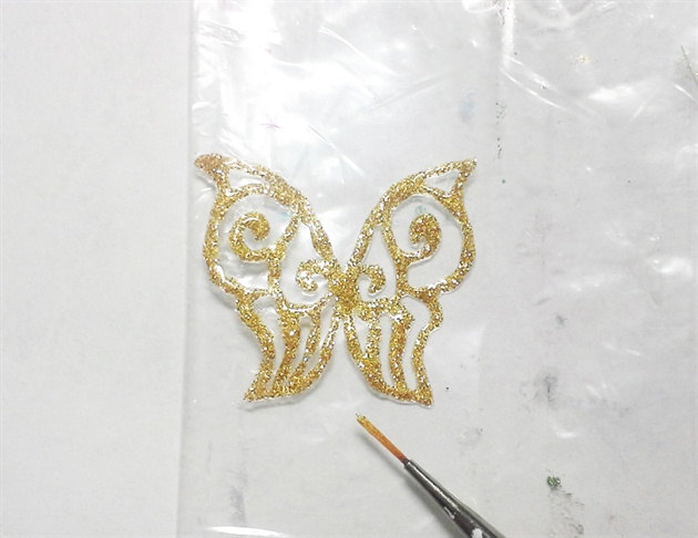 On a piece of plastic, paint a butterfly with gold glitter gel and cure. Apply a layer of hard gel over the gold gel. When curing, gently fold the butterfly wings up.