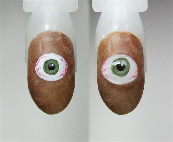For the eye, use acrylic paint to paint an eye in the center of the nail. Add some red lines to give a bloodshot effect. Let then dry then cap in clear acrylic. Top with gel topcoat to give it a glassy shiny like a real eye.