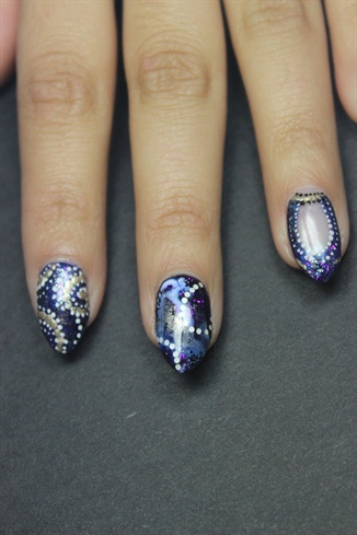 Once that dries, use a layer of gel topcoat to place on some smaller circular white glitters in a swirl shape. Add purple and black glitter to the exposed black gel polish. Cure. Seal with another layer of gel topcoat.