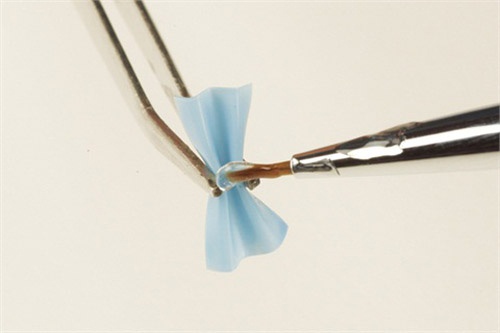 Use tweezers to pinch the center of the fold. Apply a drop of less flexible gel (Bio Sculpture S-Gel) in the center fold and cure for 30 seconds. A harder gel must be used to act as glue in order to keep the bow from unfolding.