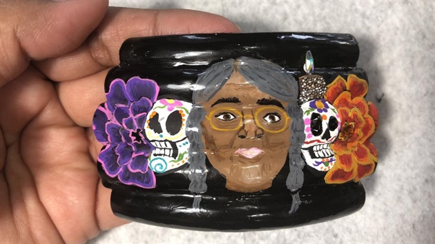 I added a darker purple acrylic paint towards the center of the flower, while still wet, I outlined with the lilac purple and blended the two together. I also added the eyes, nose, and mouth to my sugar skull along with some colorful detailing.